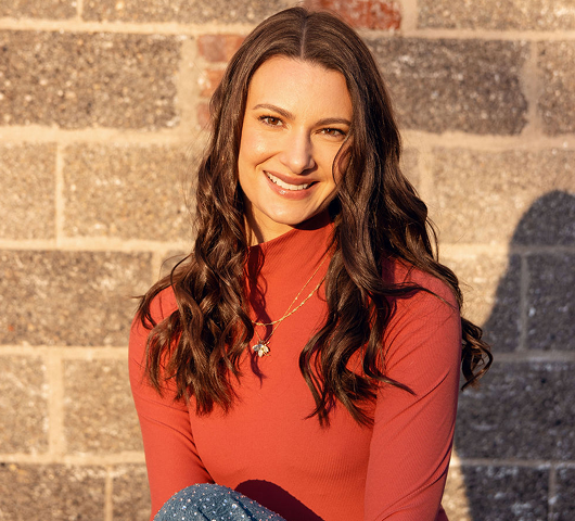 An image of Chelsea Alban, offering deep chart-based emotional support, with a natural stone wall as the backdrop