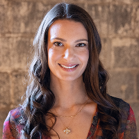 Chelsea Alban, founder of Cosmic Counseling, standing against a light-brown stone wall, offering astrology-based therapeutic services